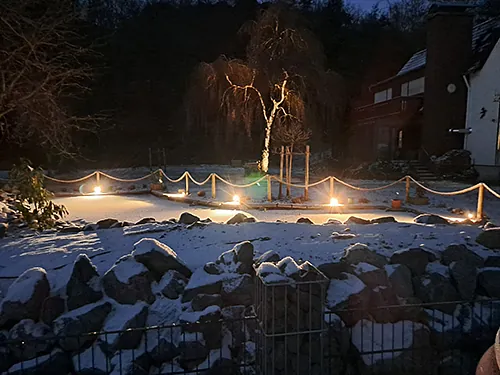 Ein beleuchteter Zaun, der im Schnee steht, strahlt eine warme Atmosphäre in der winterlichen Landschaft aus. 