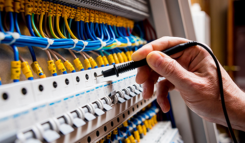 Eine Person arbeitet mit einem Werkzeug an einem elektrischen Schaltschrank. 