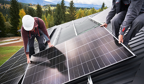 Zwei Männer installieren ein Solarpanel auf einem Dach. 