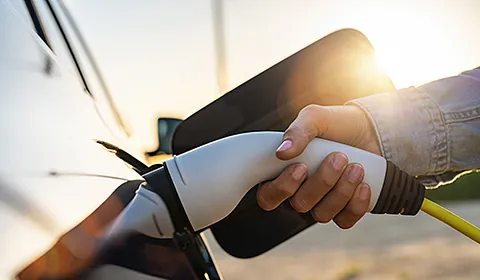 Eine Person steckt ein Ladekabel in ein Elektroauto. 
