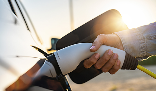 Eine Person steckt ein Ladekabel in ein Elektroauto. 
