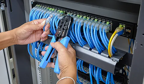 Eine Person verbindet Kabel mit einer Zange an einem Server. 