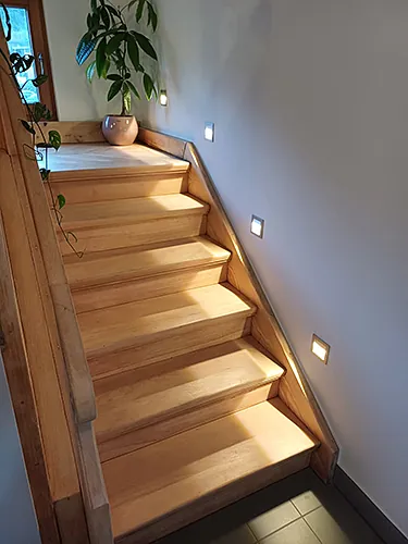 Eine hölzerne Treppe mit integrierten Lichtern, die eine warme und einladende Atmosphäre schafft. 